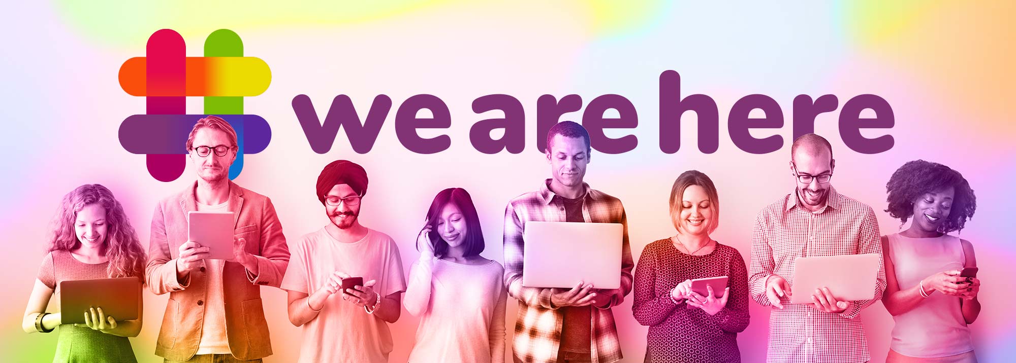 A diverse group of people standing agains at wall looking at their own digital devices with the "#wearehere" logo behind them. 